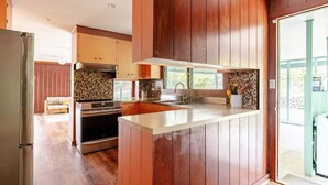 A modern kitchen with wooden cabinets, a stainless steel refrigerator, and a large island. - Kona Farm Stay - Amazing Ocean and Sunset Views (Kailua-Kona)