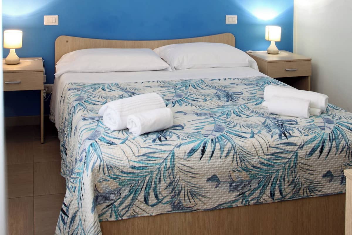 A neatly made bed with a tropical leaf-patterned bedspread, two white pillows, and two bedside lamps on wooden nightstands.