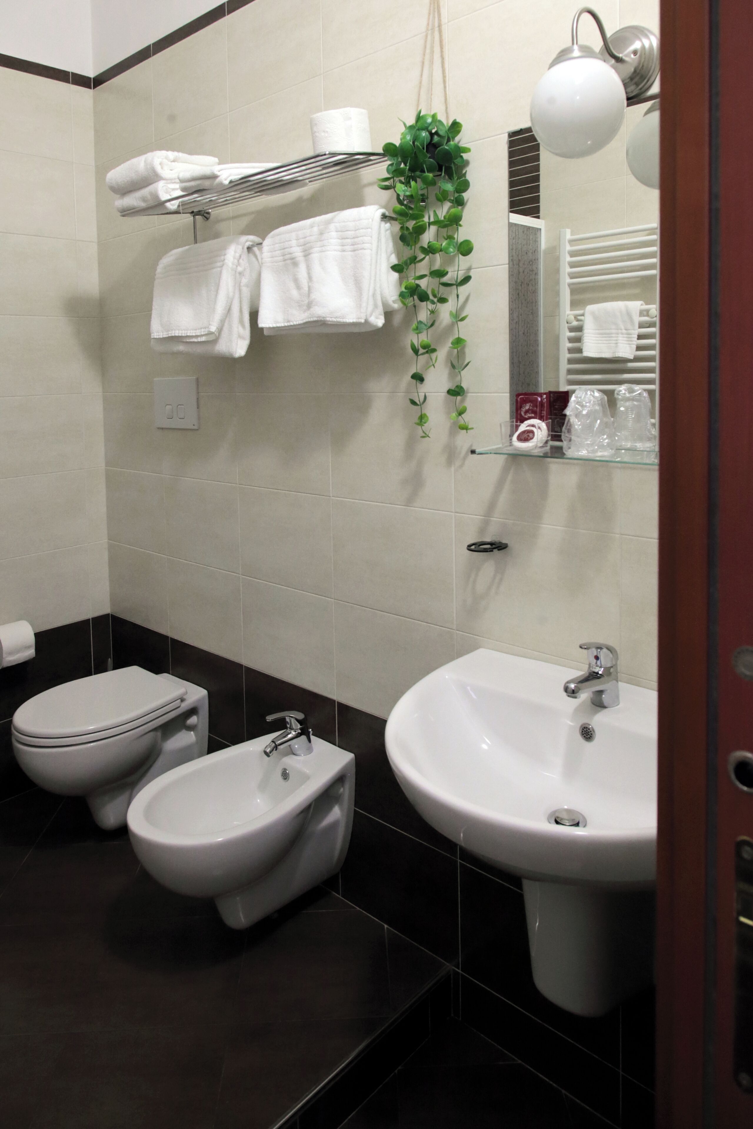 Et badeværelse med bidét, håndvask og et håndklædestativ med foldede håndklæder.