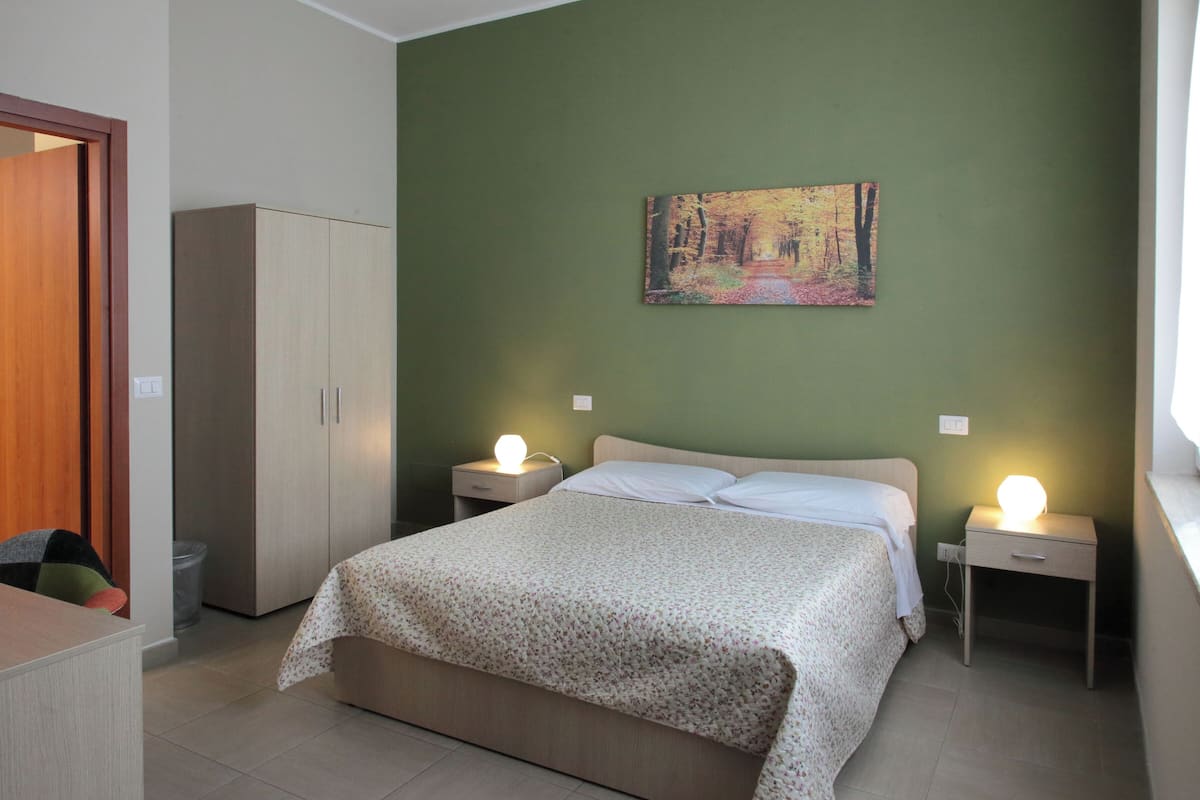 A bedroom with a bed, two bedside tables with lamps, a wardrobe, and a painting on the wall.