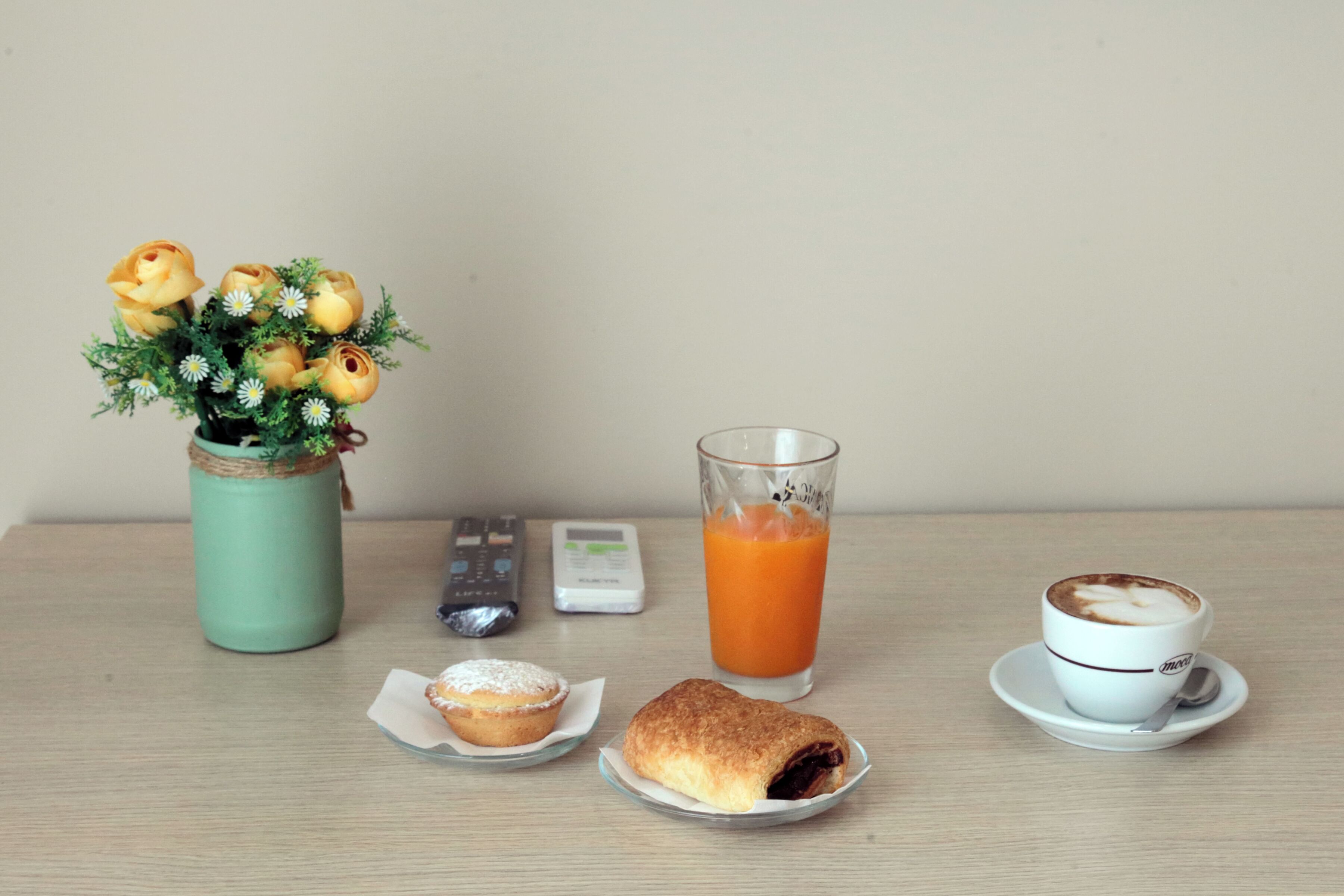 A table with a muffin, a pastry, a glass of orange juice, a cup of coffee, and a vase of flowers.