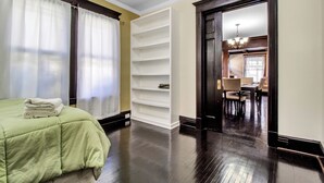 Une chambre d’hôtel avec un lit, une étagère blanche et un coin repas visible à travers une porte ouverte.