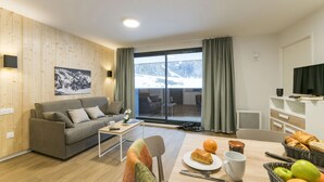 A modern living room with a grey sofa, a coffee table, and a dining area with a table set for breakfast. - Ski aux pieds ! Studio moderne + vue imprenable (Piau-Engaly)