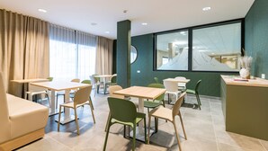 A modern dining area with multiple tables and chairs, a sofa, and a large window with a view of mountains. - Ski aux pieds ! Studio moderne + vue imprenable (Piau-Engaly)