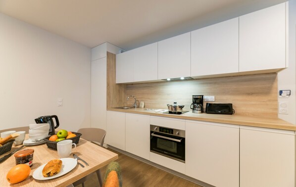 A modern kitchen with white cabinets, a wooden countertop, a built-in oven, and a coffee maker.