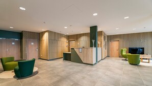 A modern lobby with a reception desk, seating area, and wooden panel walls. - Studio cosy au pied des pistes | Piscine + sauna (Piau-Engaly)