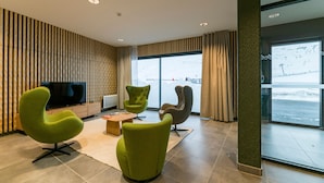 A modern lobby with green chairs, a wooden coffee table, and a large window offering a view of a snowy landscape. - Studio cosy au pied des pistes | Piscine + sauna (Piau-Engaly)