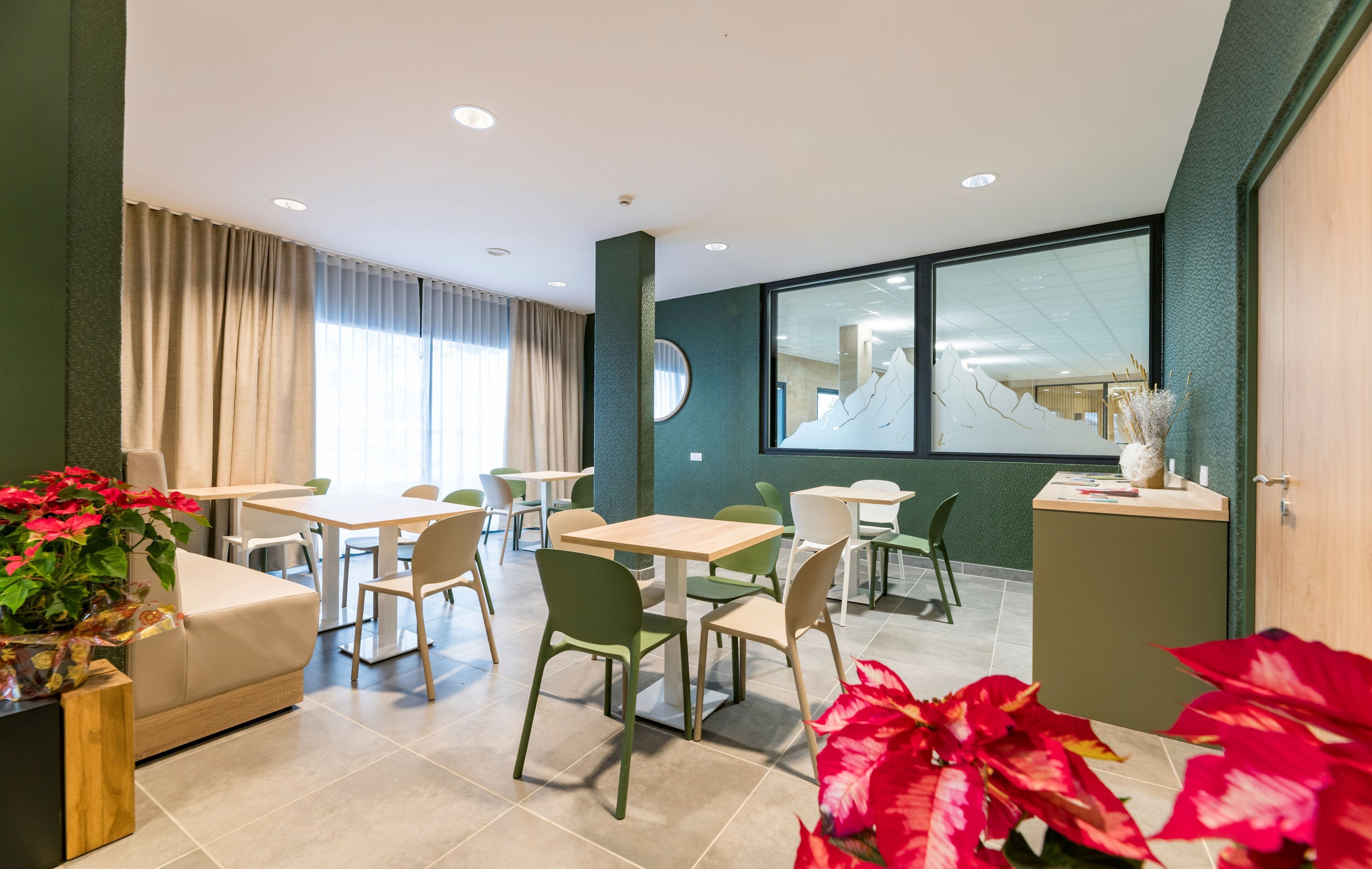 A modern hotel room with a dining area, green walls, and large windows.