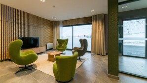 A modern lobby with green chairs, a wooden coffee table, and a large window offering a view of a snowy landscape.