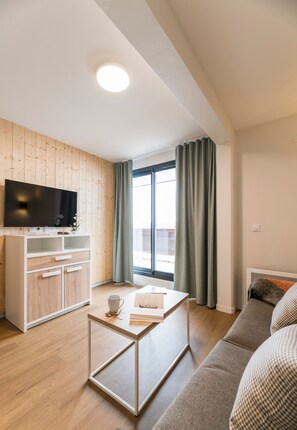 Una sala de estar moderna con televisor de pantalla plana, armarios de madera, una mesa de centro de vidrio y un sofá.