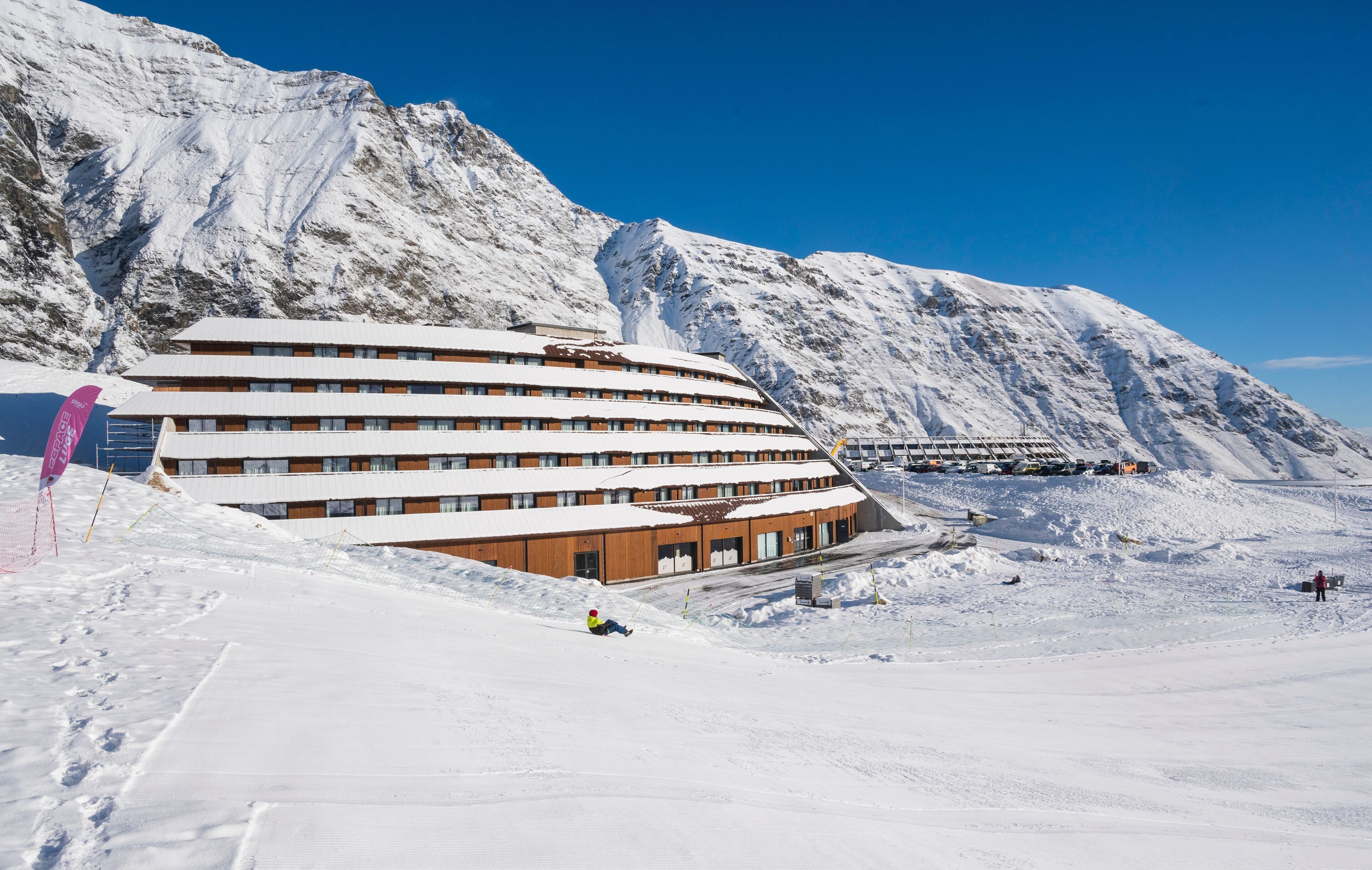 Ett hotell med flera våningar, en skidbacke i förgrunden och ett berg i bakgrunden.