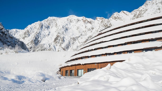 A snow-covered mountain with a wooden building featuring a curved roof.