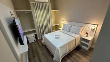 A neatly arranged hotel room with a bed, bedside tables, a TV, and a curtain.