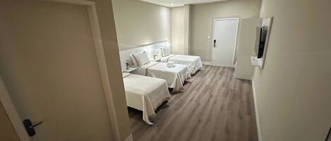 Una habitación de hotel con tres camas, un televisor y una puerta.