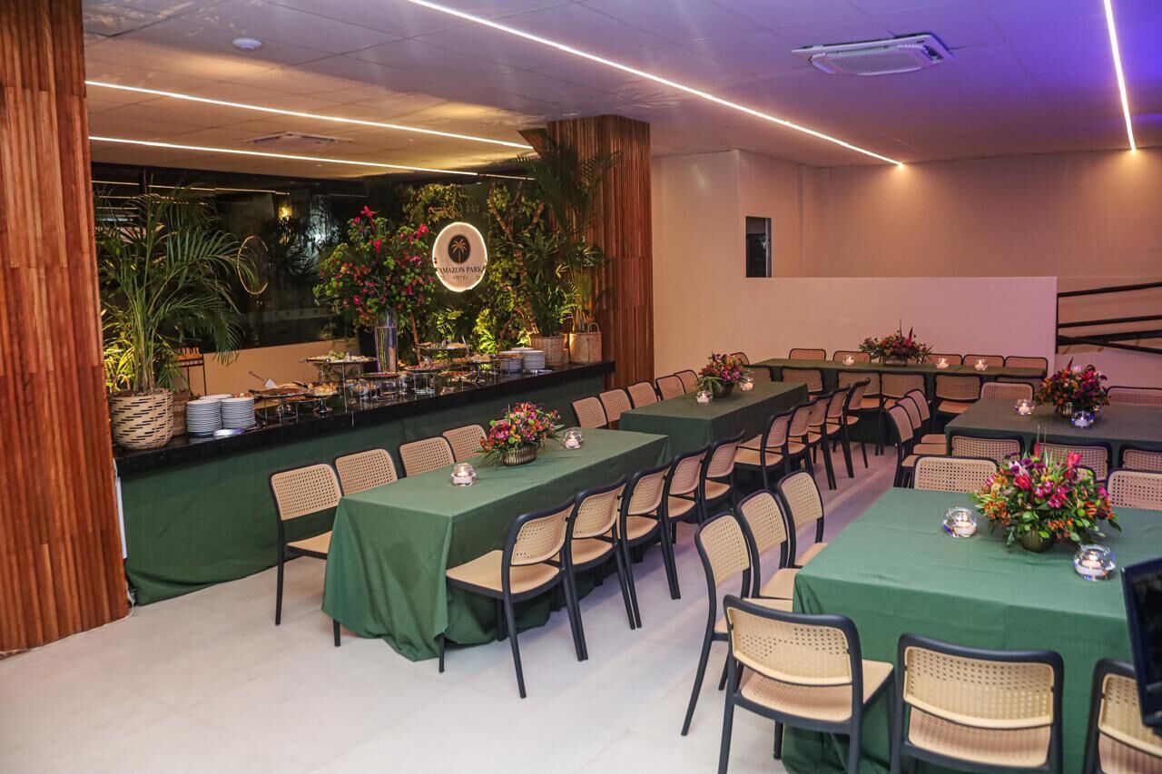 A conference room with long tables, chairs, and a backdrop of plants and a circular logo.