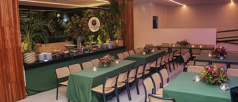 A conference room with long tables, chairs, and a backdrop of plants and a circular logo.