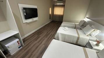 Une chambre d’hôtel équipée d’un téléviseur à écran plat fixé au mur, de deux lits avec du linge de lit blanc, d’une petite table avec une lampe et d’un mini-bar.