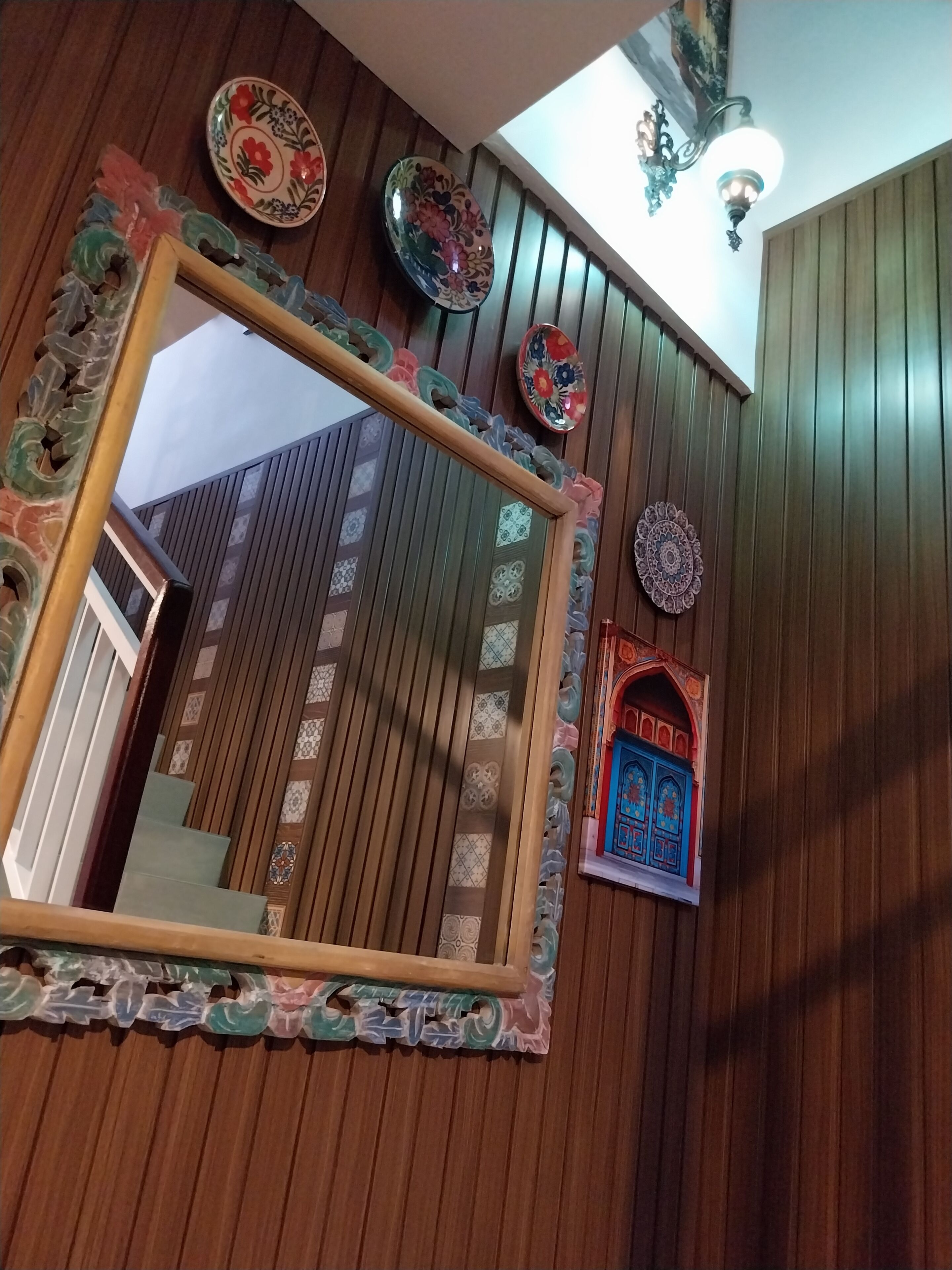Une pièce dotée d’un grand miroir, d’assiettes décoratives et d’une petite fenêtre aux motifs complexes.