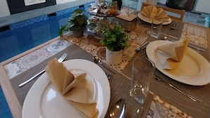 A dining area with a pool view, featuring a table set with plates, napkins, and cutlery. - Azura Villas Nusa Dua Bali (Nusa Dua)