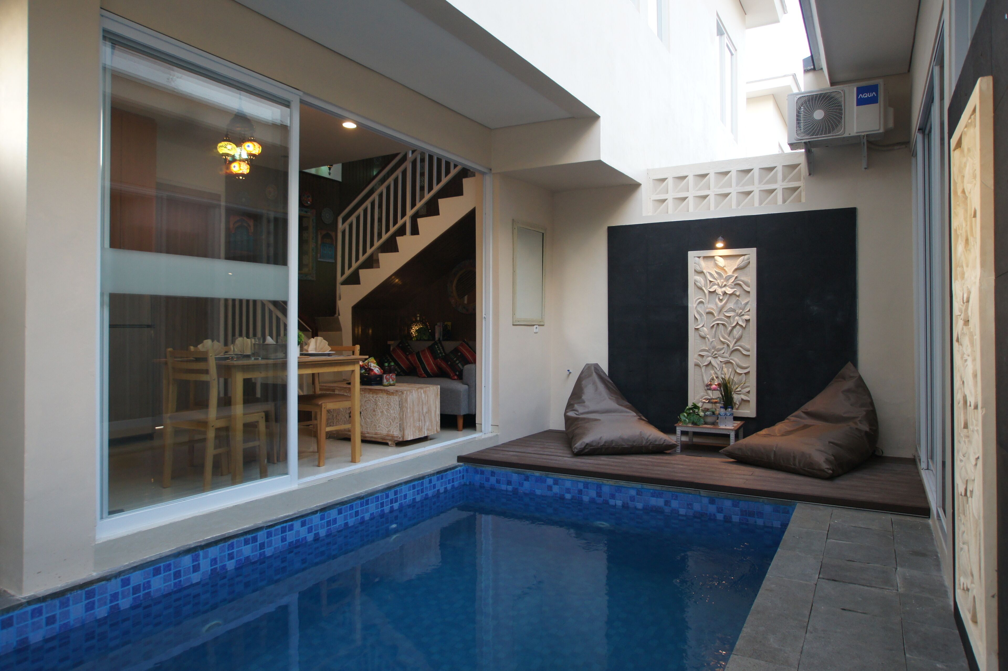 Uma área de piscina moderna com porta de vidro que dá para uma sala de jantar, uma escadaria e uma parede decorativa.