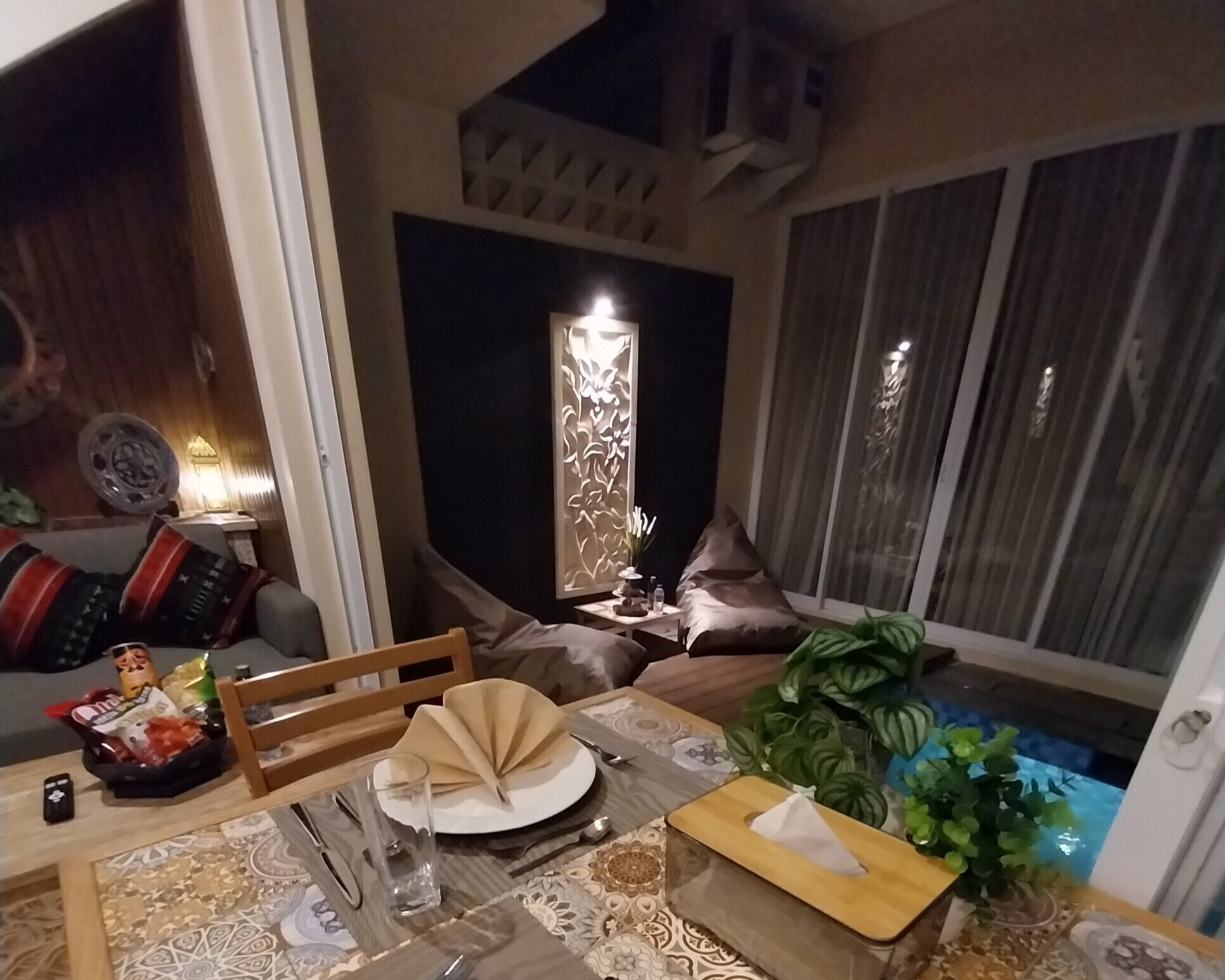 Ένας χώρος τραπεζαρίας με ένα τραπέζι στρωμένο για δύο άτομα, ένα διακοσμητικό πάνελ στον τοίχο και ένα παράθυρο με κουρτίνες.