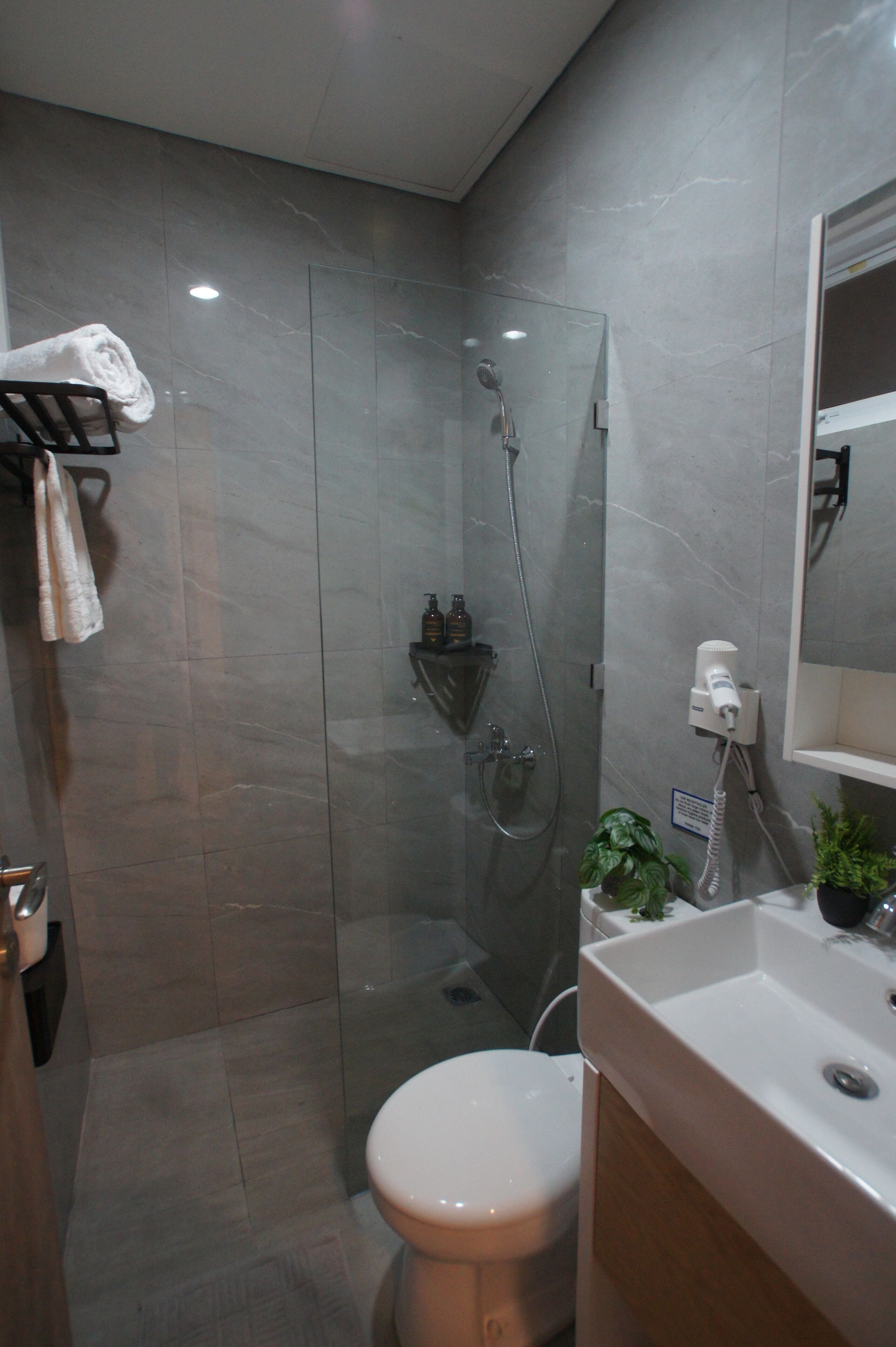 Un baño moderno con ducha acristalada, inodoro blanco y lavamanos con espejo.