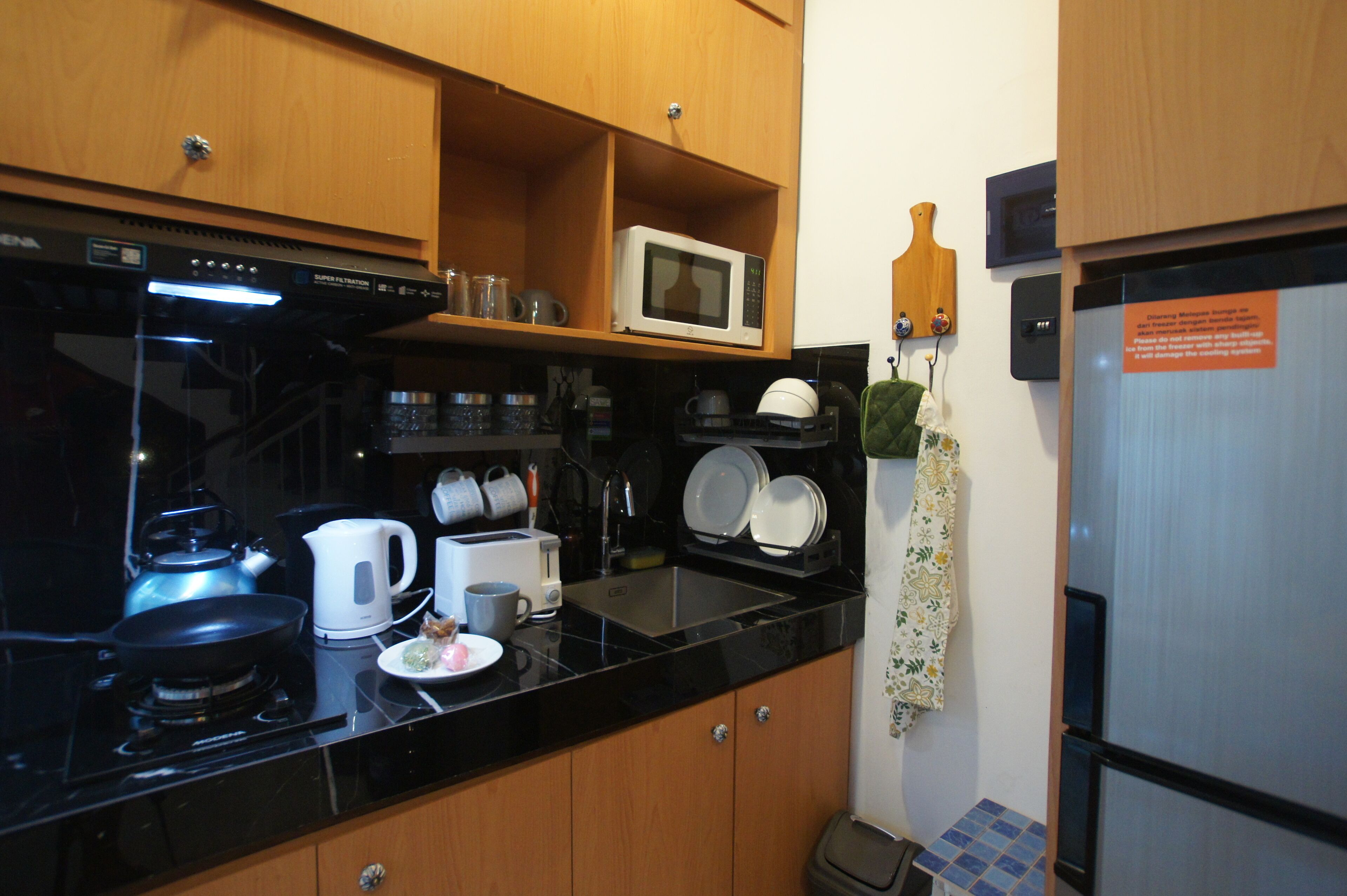 A compact kitchen with a black countertop, a microwave, a kettle, and a sink.