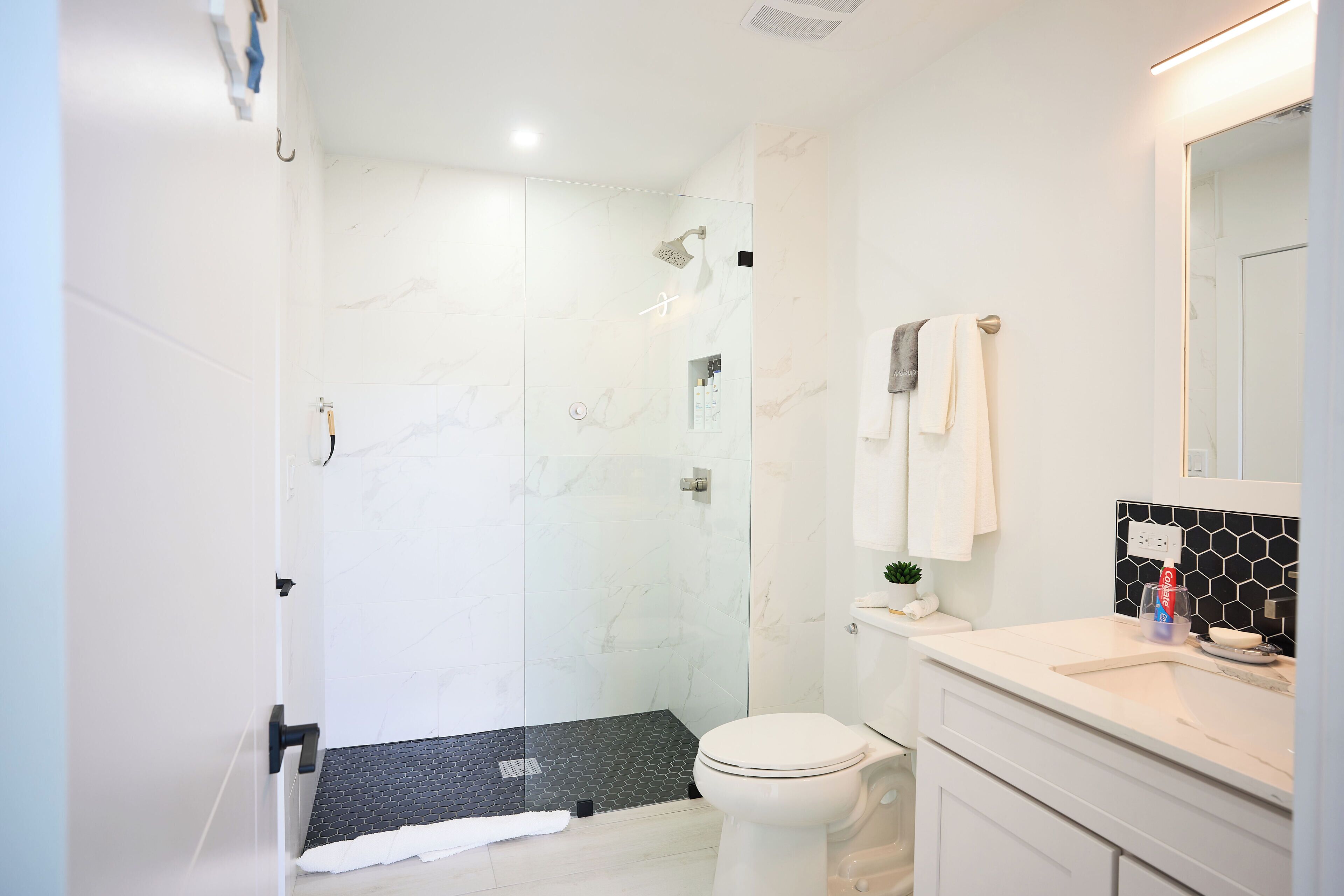 Un baño moderno con ducha de vidrio, inodoro y tocador con espejo.