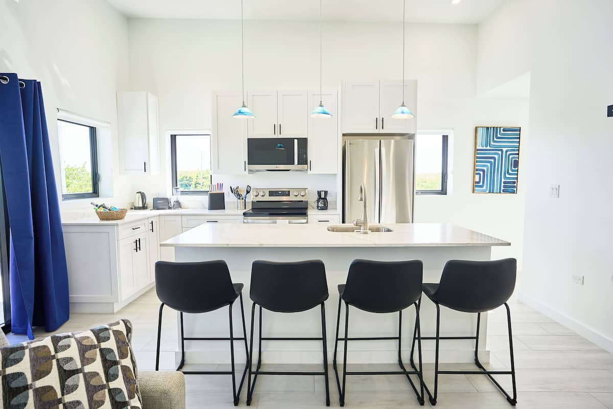 A modern kitchen with white cabinets, a central island with bar stools, a microwave, oven, and refrigerator.