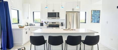 A modern kitchen with white cabinets, a central island with bar stools, a microwave, oven, and refrigerator.