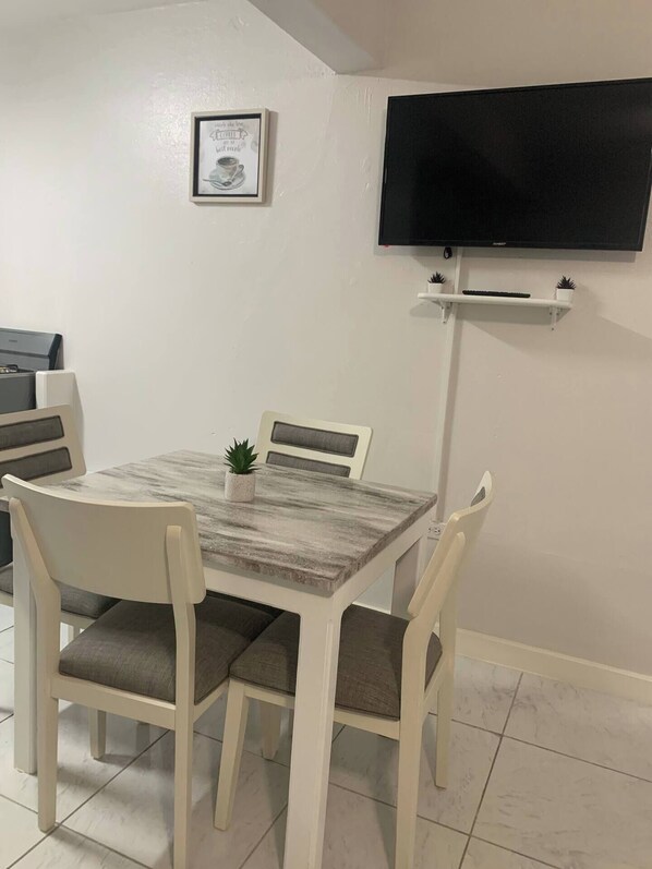 Un coin repas comprenant une table, des chaises, une petite plante en pot, un tableau encadré accroché au mur et un téléviseur fixé au mur.