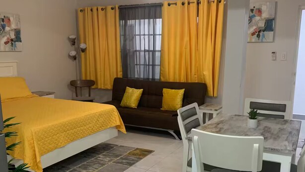 A hotel room with a bed, a sofa, a dining table with chairs, and a ceiling fan.