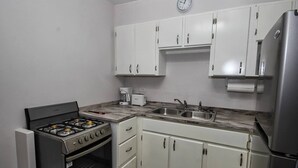 A compact kitchen with white cabinets, a stainless steel refrigerator, a gas stove, a coffee maker, and a sink. - The Castle ᴶ (Philipsburg)