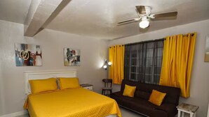 A bedroom with a bed, a sofa, a ceiling fan, and a window with yellow curtains.