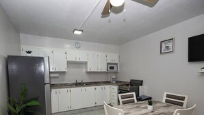 A compact kitchen with white cabinets, a stainless steel refrigerator, a microwave, a stove, and a dining table with chairs. - The Castle ᴳ (Philipsburg)