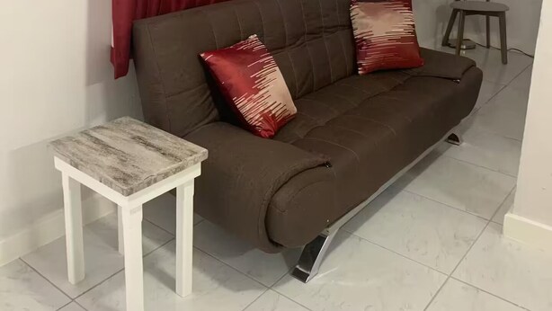 Ein Wohnzimmer mit einem braunen Sofa, zwei roten Kissen, einem kleinen weißen Tisch und einer Stehlampe.