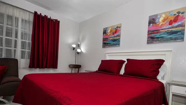 A bedroom with a large bed, red curtains, a nightstand, a lamp, and two paintings on the wall. - The Castle ᴳ (Philipsburg)