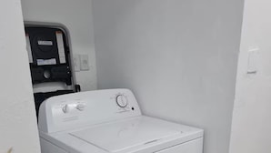 A compact, white front-loading washer and dryer unit in a corner of a room with a tiled floor and a small potted plant. - The Castle ᴳ (Philipsburg)