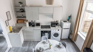 Une cuisine moderne avec des meubles blancs, une table à manger pour quatre personnes et un lave-linge.