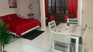 Une chambre à coucher avec un lit, une table à manger avec des chaises, un canapé et une fenêtre avec des rideaux.