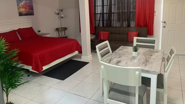 A bedroom with a bed, a dining table with chairs, a sofa, and a window with curtains. - The Castle ᴷ (Philipsburg)