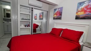 A bedroom with a red bedspread, white headboard, and two red pillows. There are two paintings on the wall, a closet with a sliding door, and a bathroom visible in the background. - The Castle ᴷ (Philipsburg)