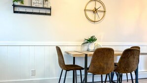 Un comedor con una mesa de madera, cuatro sillas marrones, un reloj en la pared y un estante con adornos.