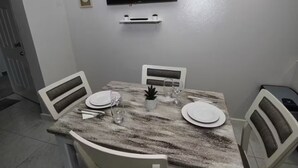 A dining area with a table set for two, a flat-screen TV mounted on the wall, and a small shelf below it. - The Castle ᴵ (Philipsburg)