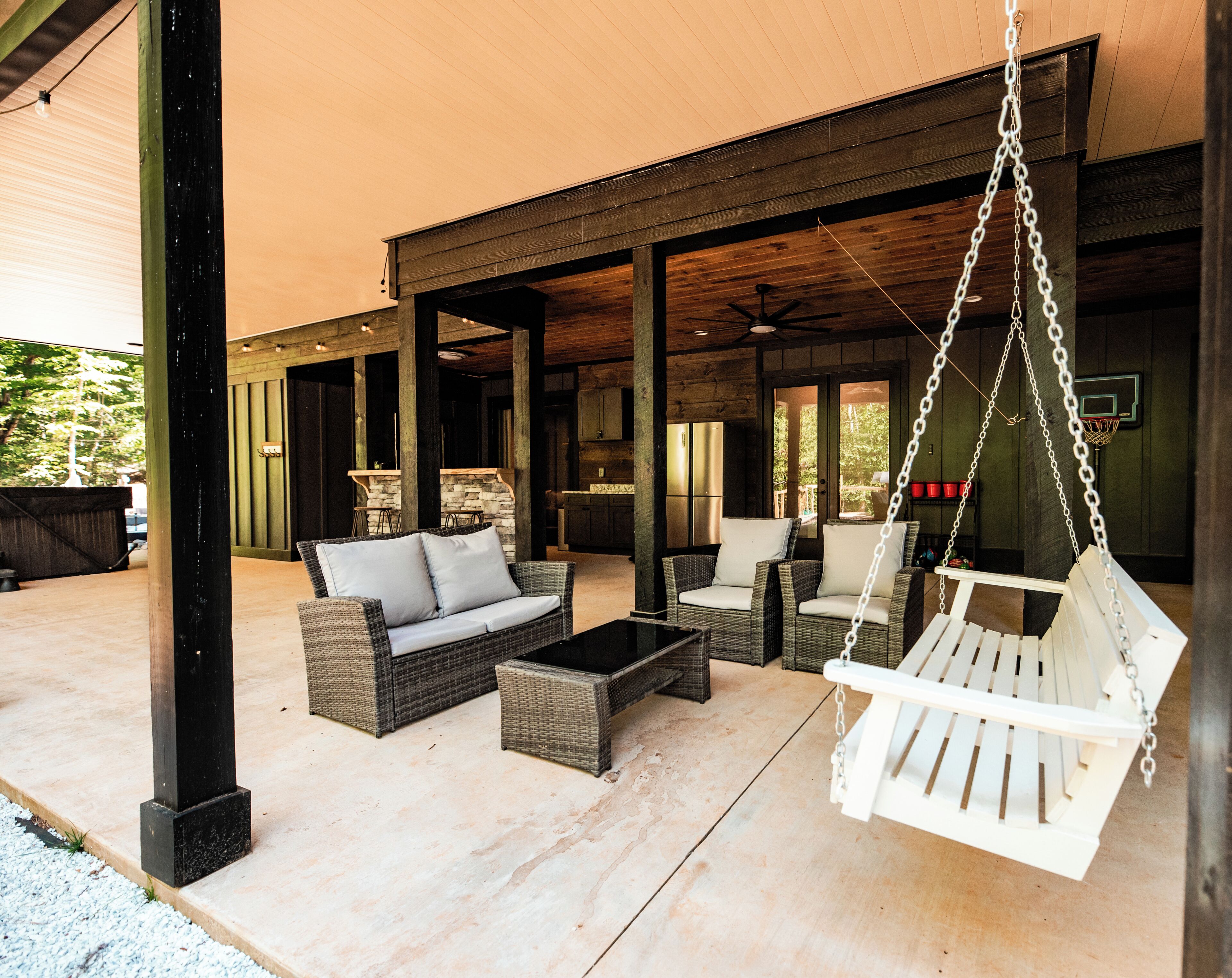 An outdoor patio area with wicker furniture, a hanging swing, and a basketball hoop.