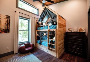 Une pièce avec un lit en mezzanine, un fauteuil rouge, une commode et une fenêtre avec des rideaux.