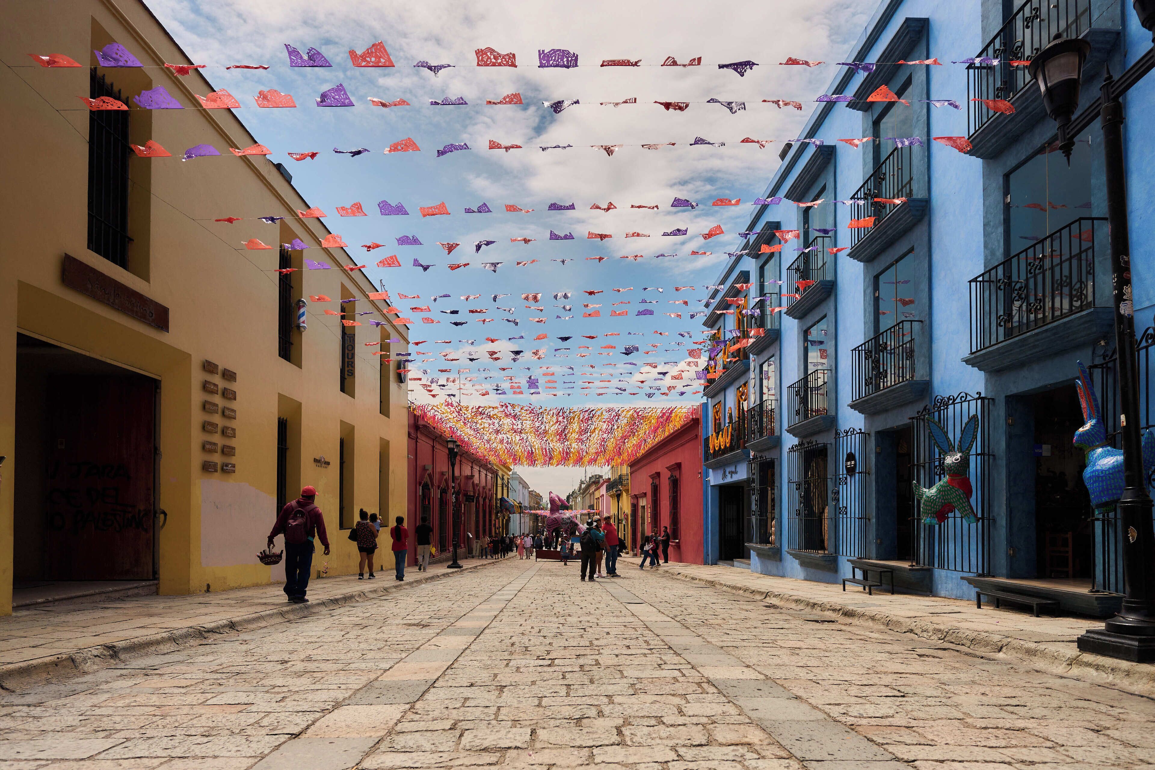 Una calle adoquinada flanqueada por edificios coloridos, cielo despejado y ambiente festivo con adornos colgantes.