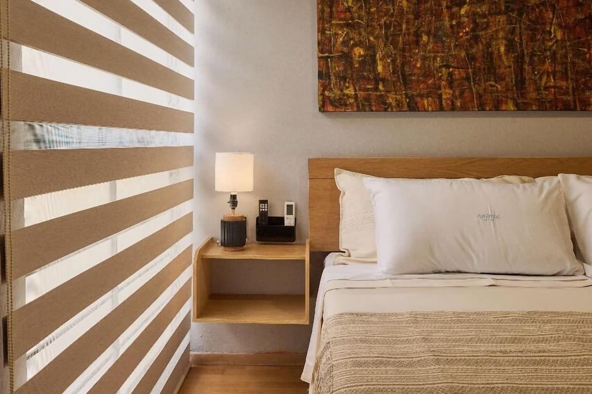 A bedroom with a bed, a nightstand with a lamp, and a large abstract painting on the wall.