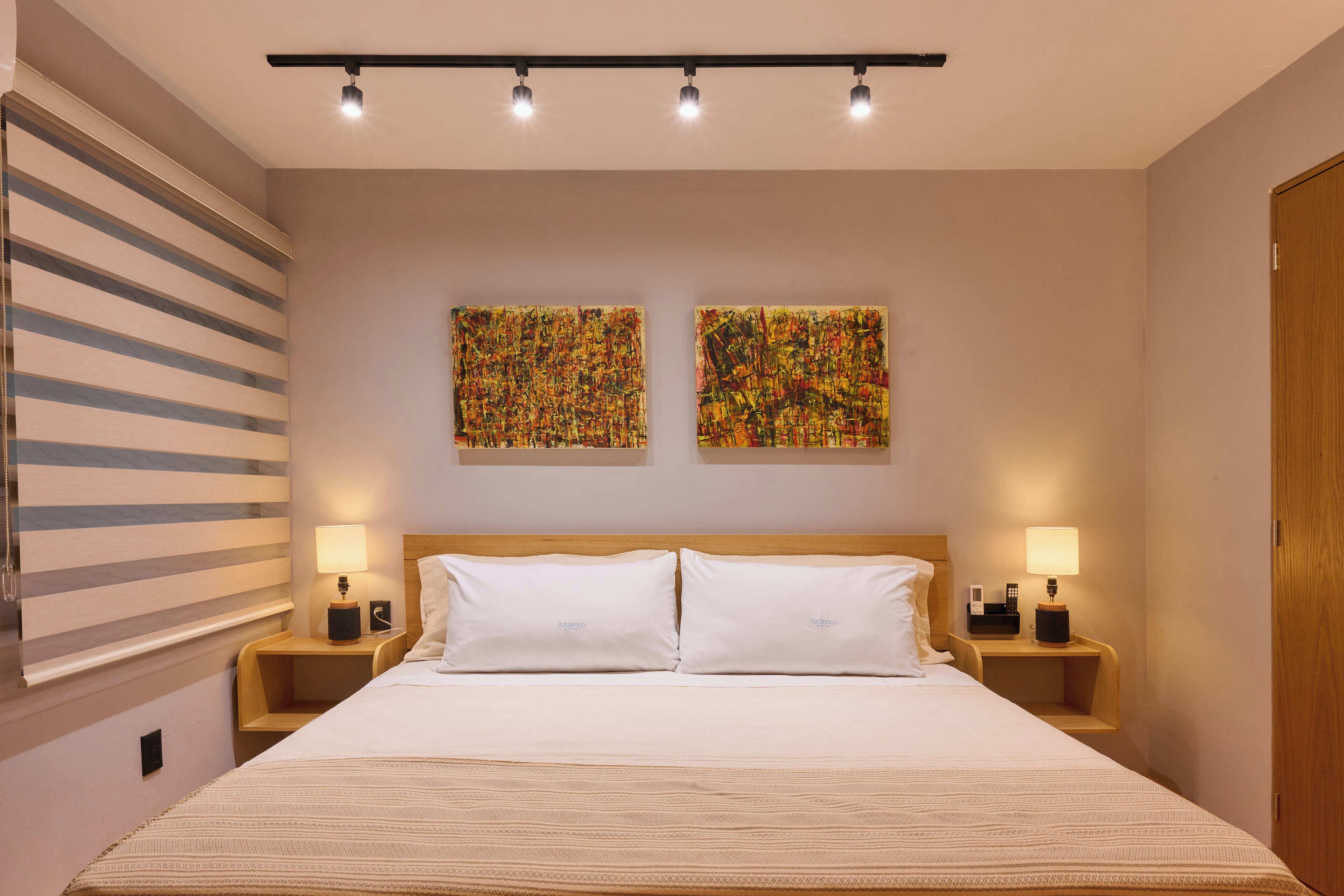 A hotel room with a large bed, two bedside tables with lamps, a wooden headboard, and two abstract paintings on the wall.