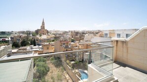 A cityscape with a prominent church tower, residential buildings, and a rooftop pool area. - Ghajnsielem Retreat 4 Bedrooms, Panoramic Terrace (Ghajnsielem)